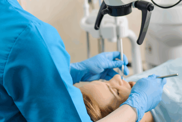 person in scrubs standing by person laying in dental chair