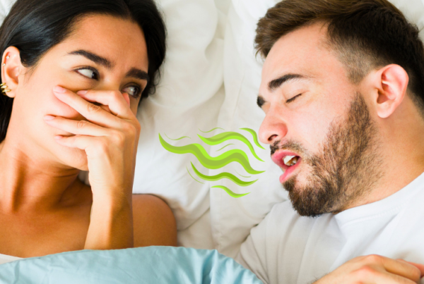 woman covering her nose facing man in bed blowing bad breath