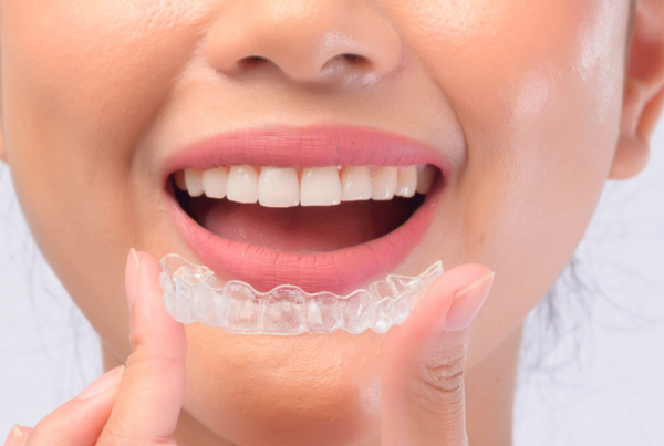 Woman holding clear aligner in front of her smile.