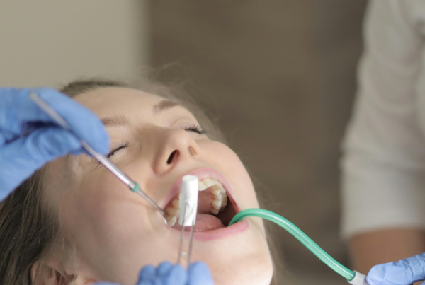 Gloved hands using dental tools in female patient's mouth.