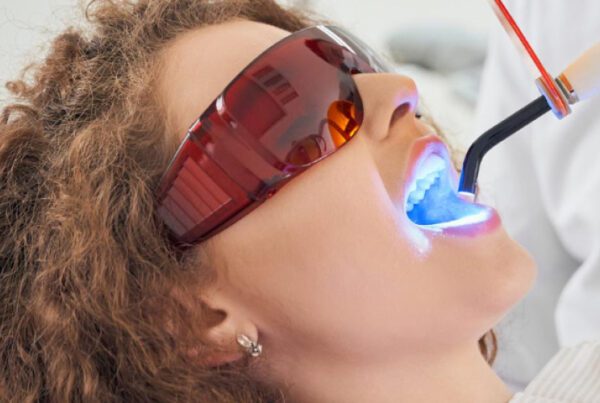 Patient receiving professional teeth whitening treatment with a blue light laser in dental office.