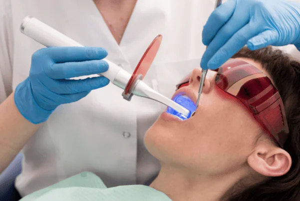 Professional teeth whitening treatment with a dental professional applying whitening gel while a bright LED light enhances the patient’s smile.